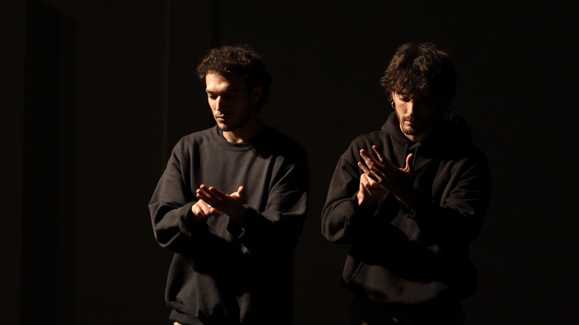 The two performers side by side, each looking down at his raised hand