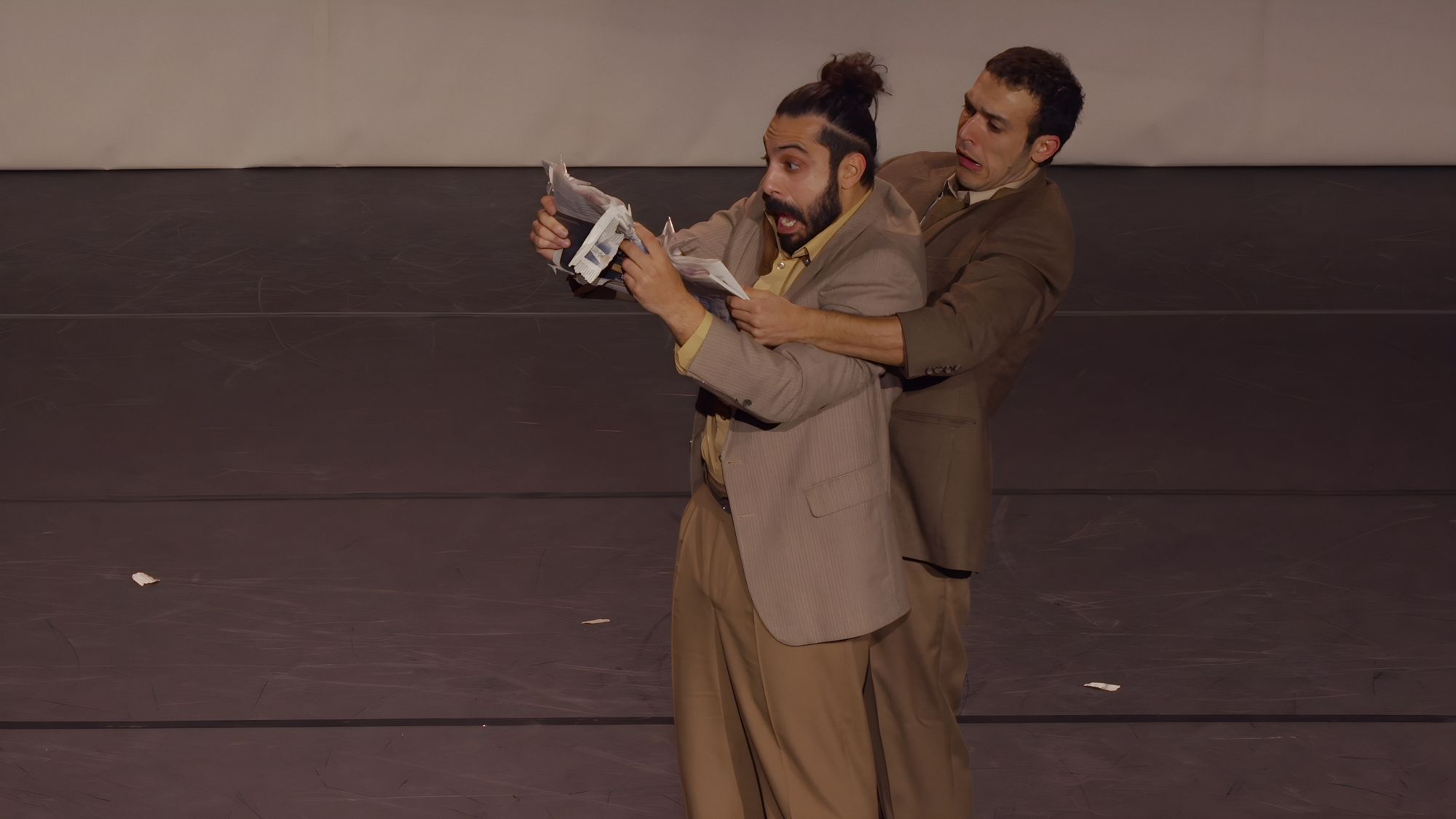 One performer reads a newspaper while the other leans over his shoulder