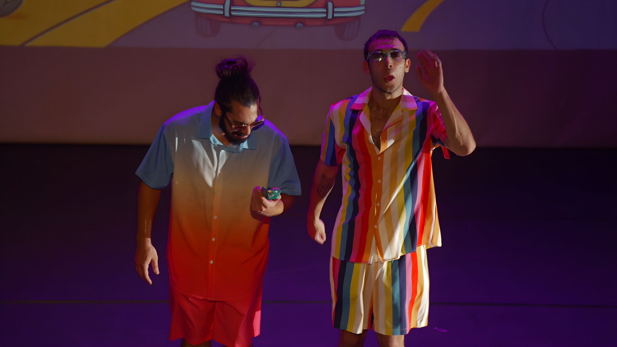The two performers in rainbow-coloured shirts under violet light