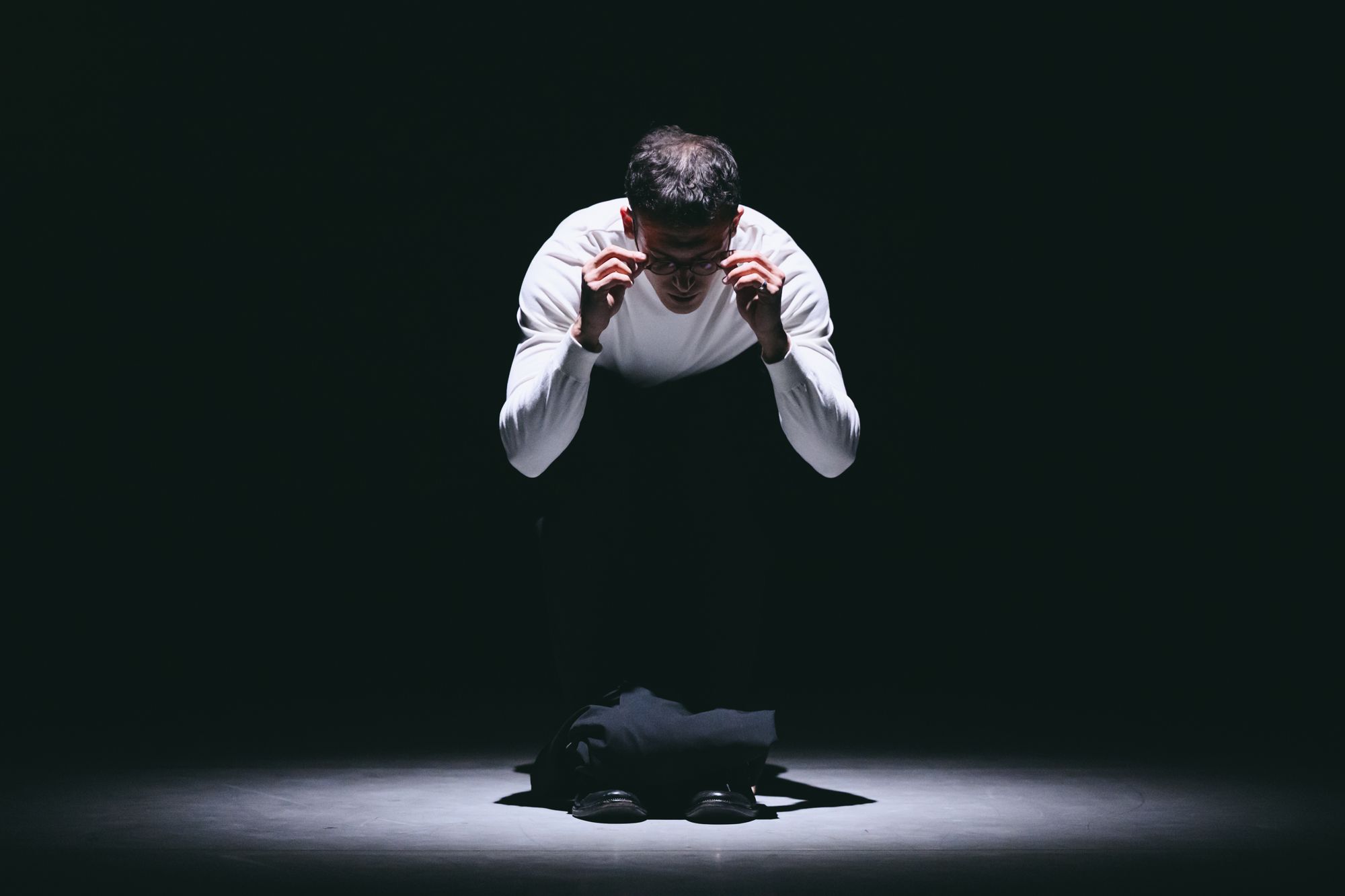 Alexandros bent forward in a spotlight, hands at his face