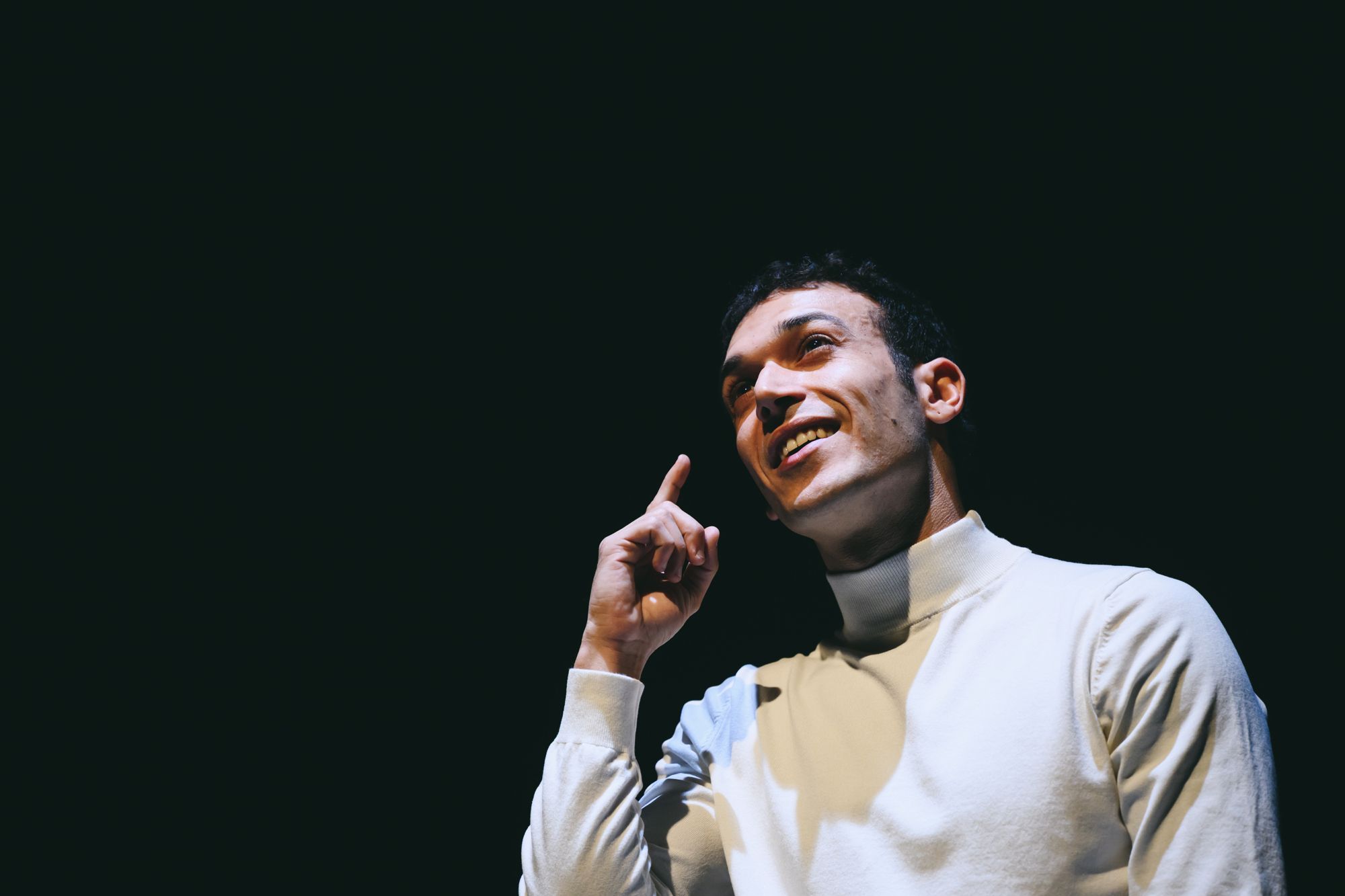Close-up of Alexandros smiling upward, one finger raised to his temple