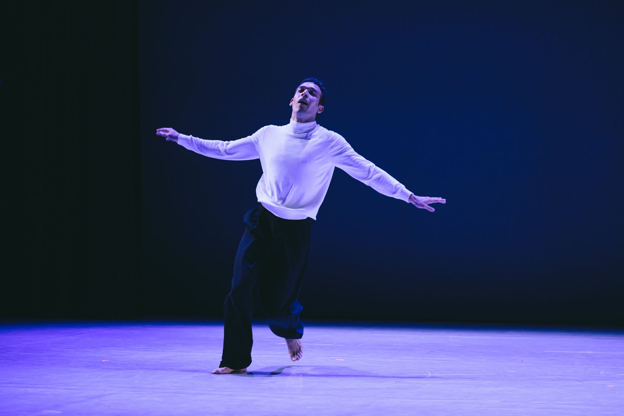 Alexandros mid-step with arms spread under blue light