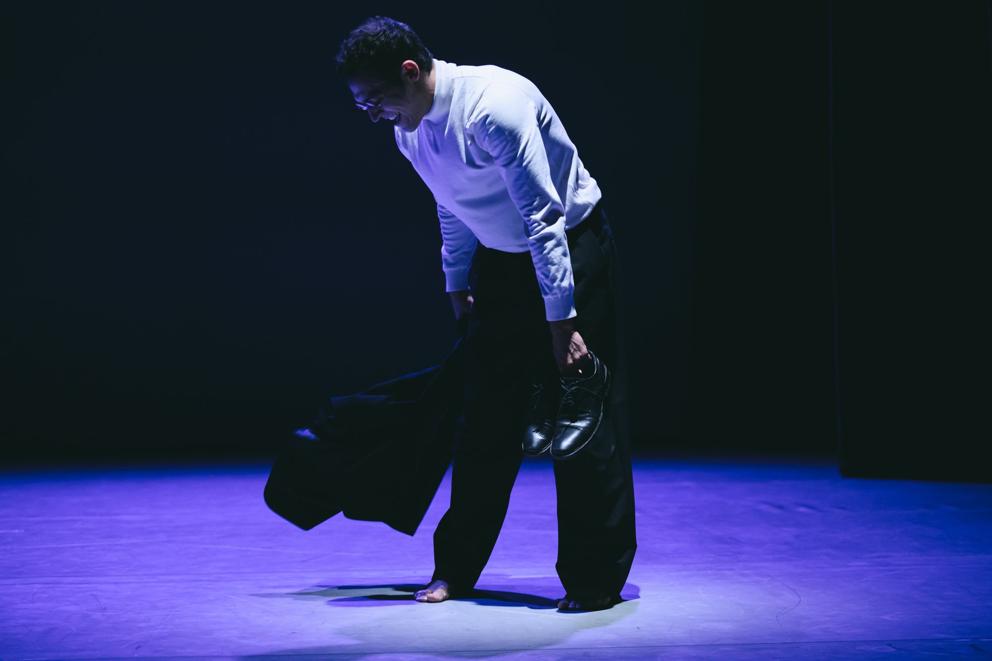 Alexandros bending to pick up a jacket under violet light
