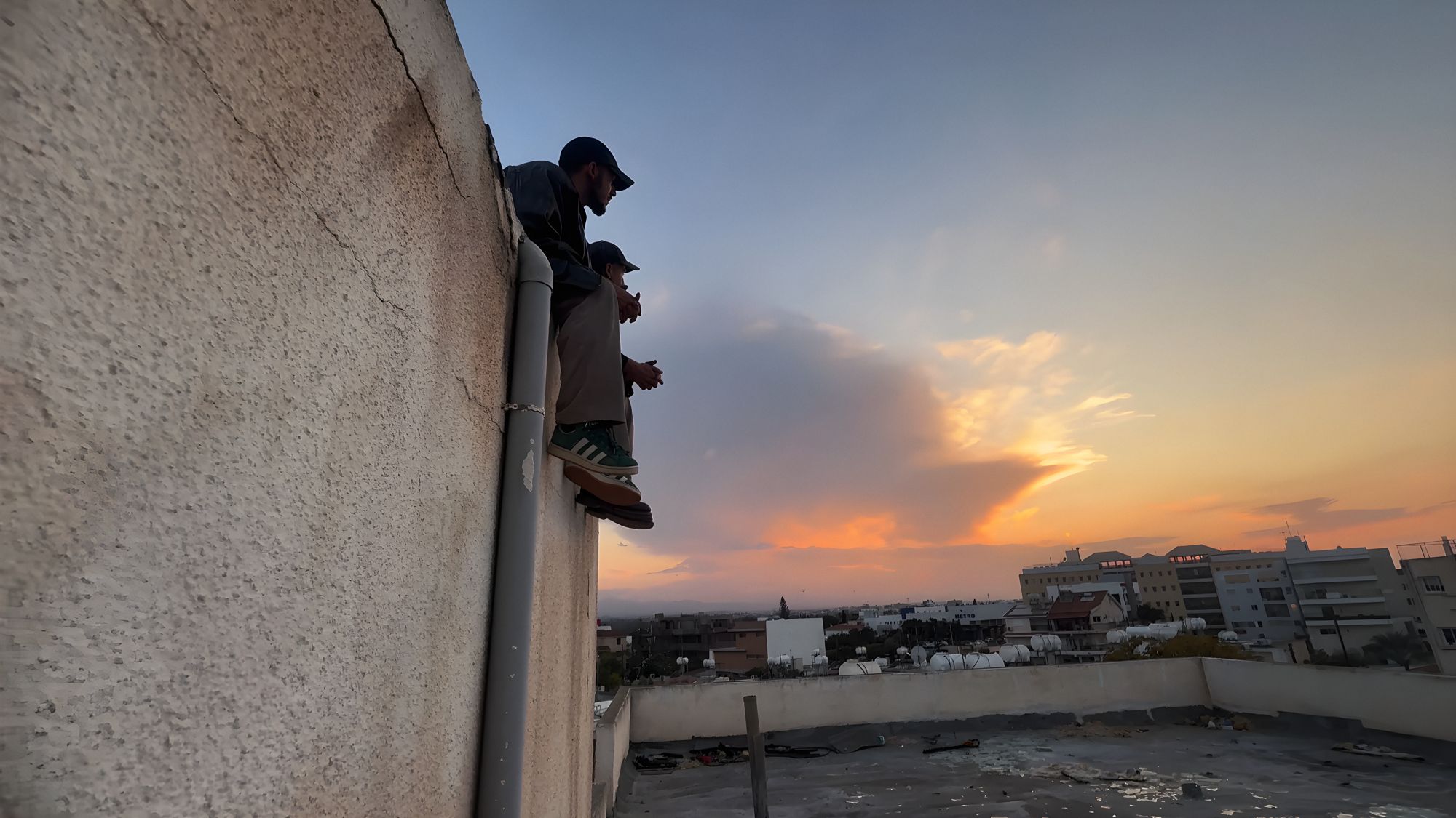 Two figures on a rooftop ledge at sunset